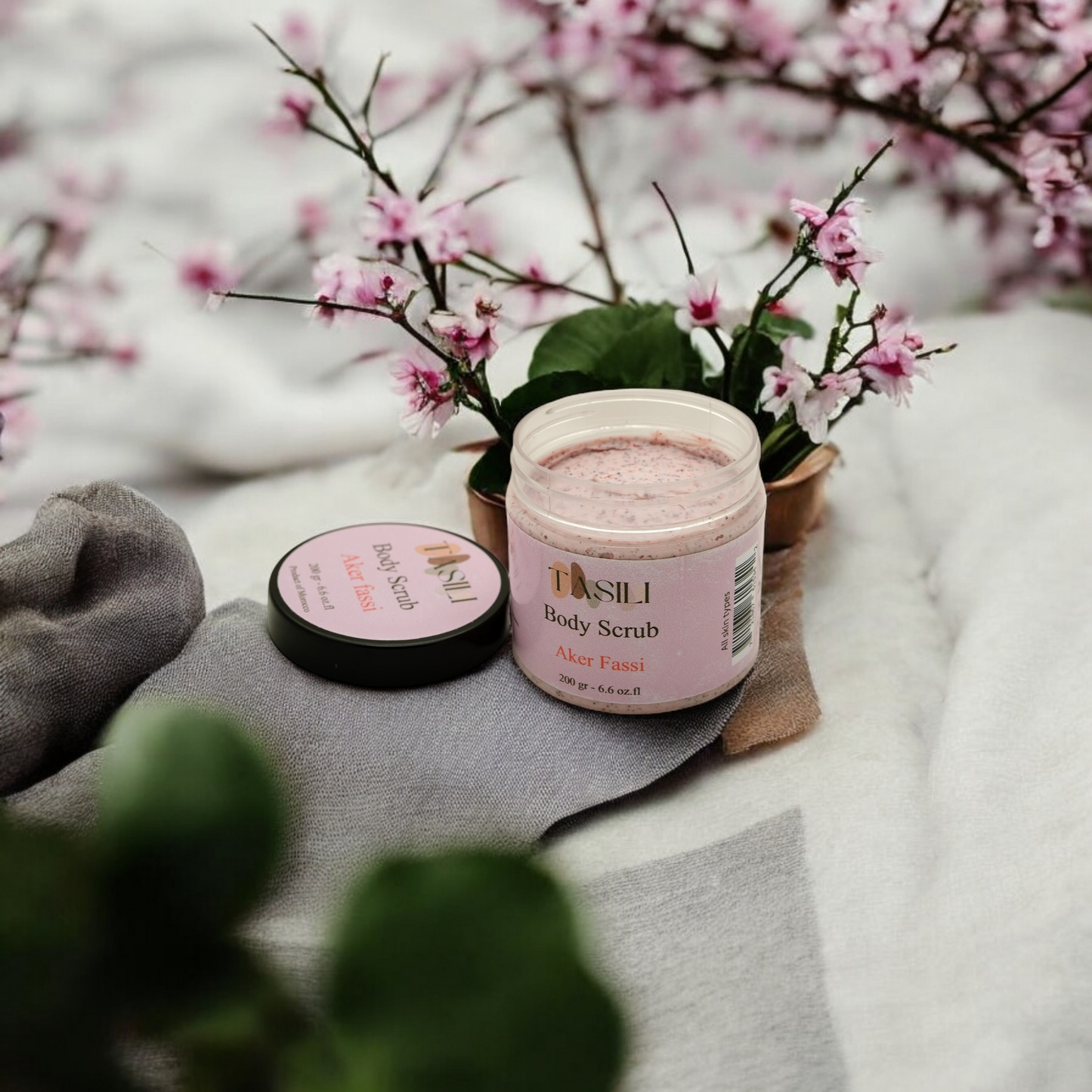 Akker Fassi Body Scrub on a towl surrounded by pink flowers 