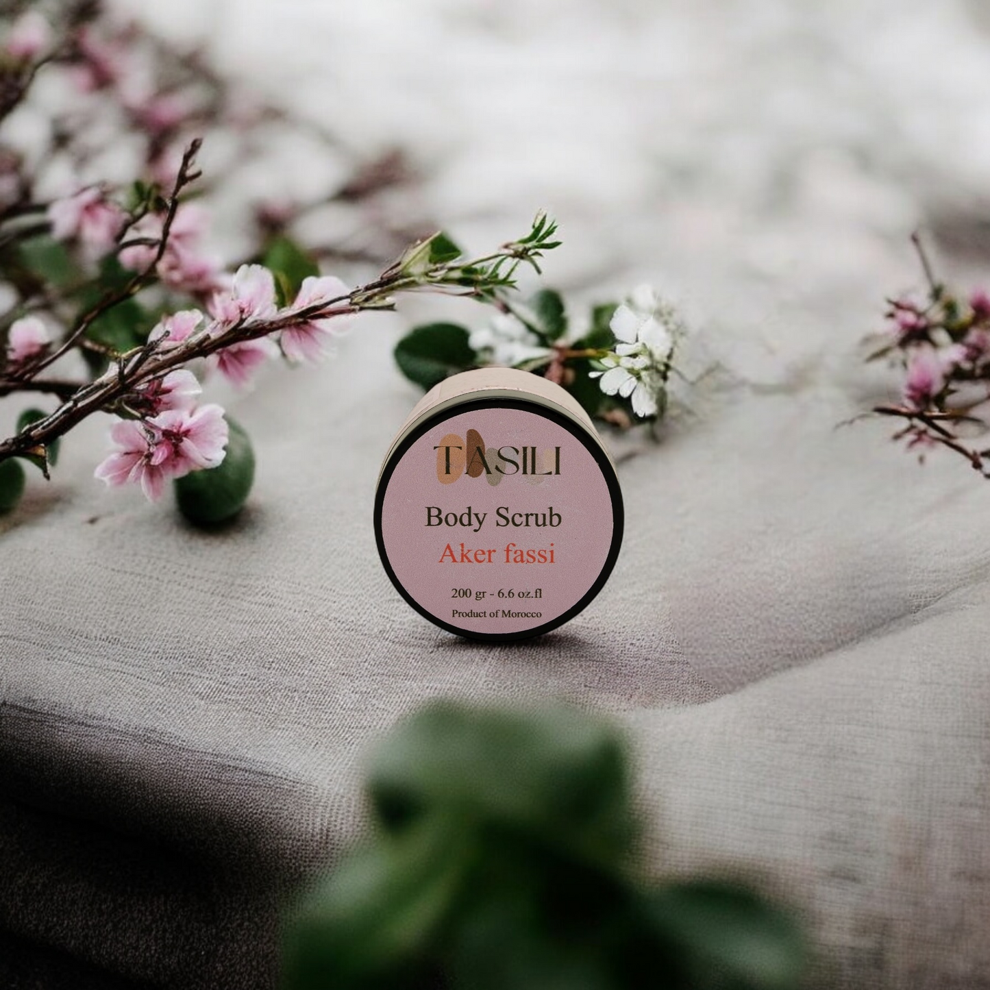 Akker Fassi Body Scrub on a towl surrounded by pink and white flowers